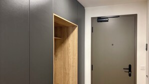 A hallway with a dark grey wall, a wooden shelf, a door with a handle, and a light fixture on the ceiling.
