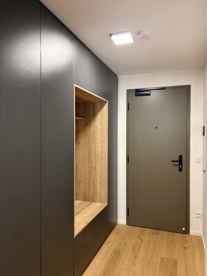 Un couloir avec un mur de couleur gris foncé, une étagère en bois, une porte avec une poignée et un luminaire au plafond.