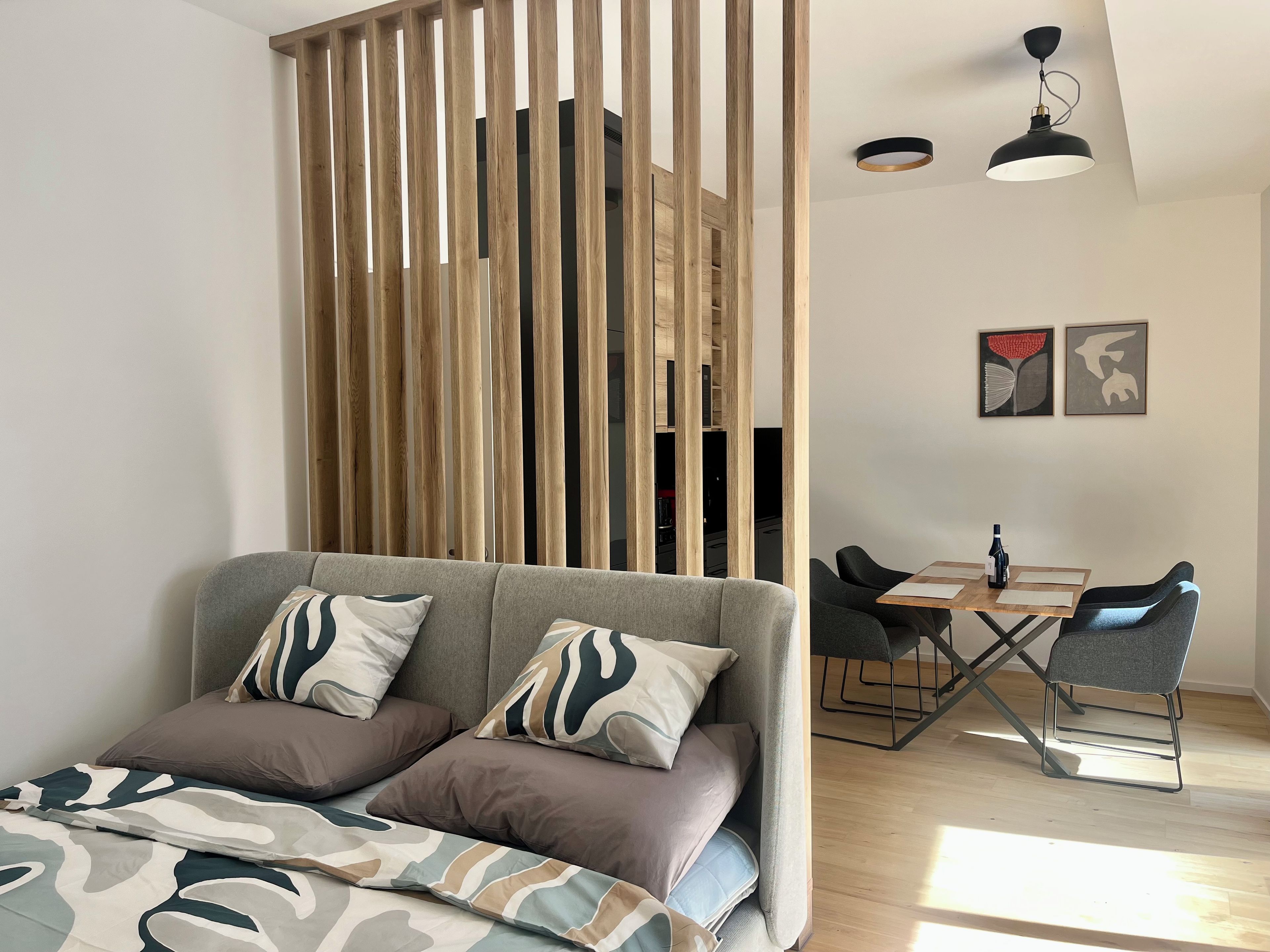 A modern living room with a sofa, a dining table with chairs, and a wooden partition.