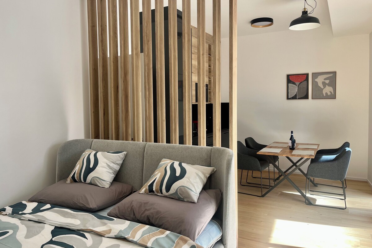 A modern living room with a sofa, a dining table with chairs, and a wooden partition.