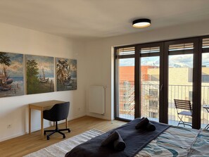 Ein Schlafzimmer mit Bett, Schreibtisch, Stuhl und Blick auf die Stadt durch große Fenster.