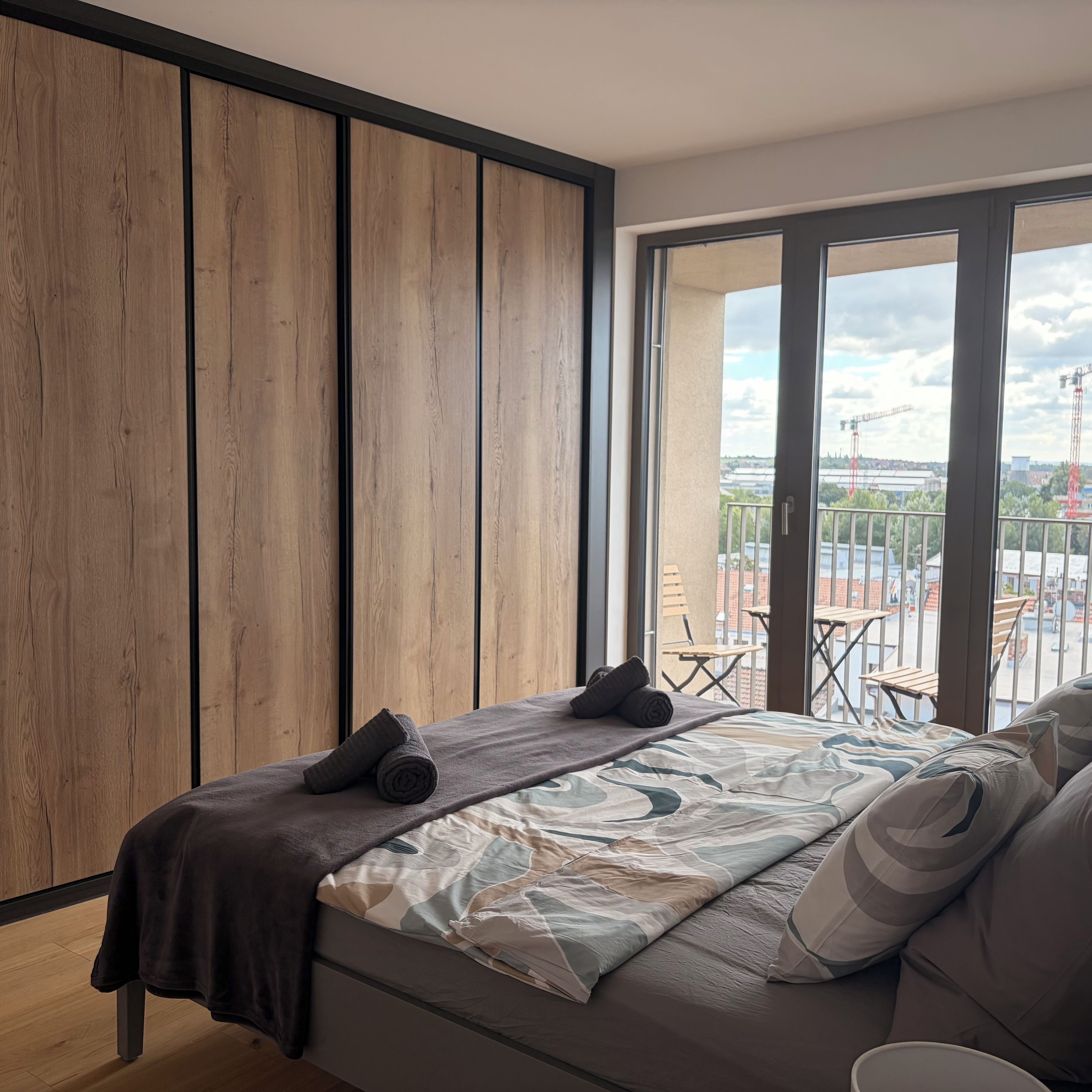 Une chambre moderne avec un grand lit, une vue sur l’extérieur et un balcon aménagé avec du mobilier d’extérieur.