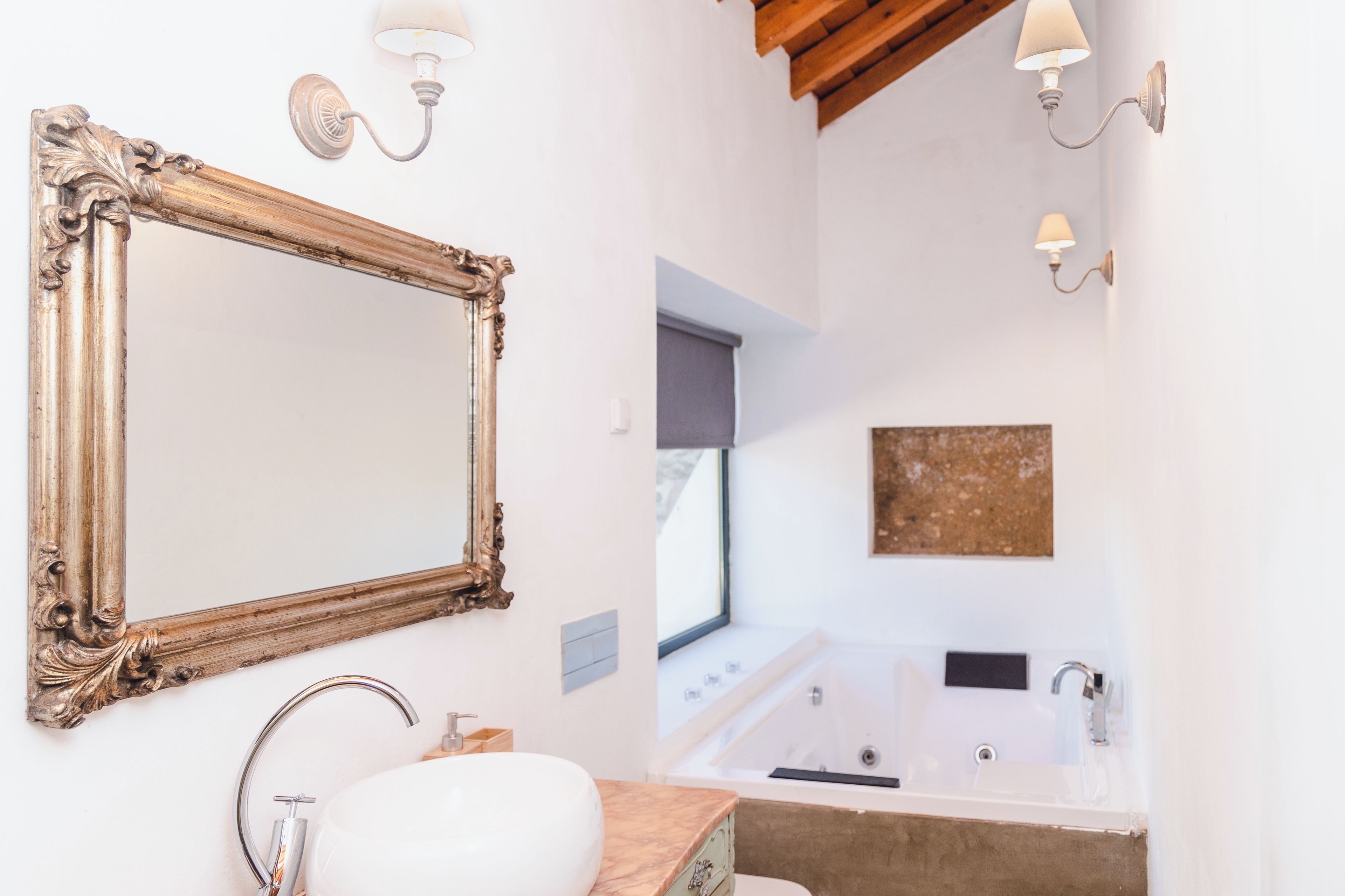 Un baño con un espejo grande, un lavamanos, una bañera y dos lámparas fijadas a la pared.