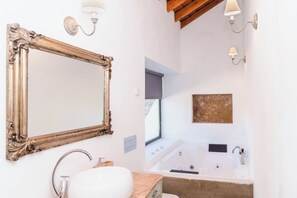 Un baño con un espejo grande, un lavamanos, una bañera y dos lámparas fijadas a la pared.