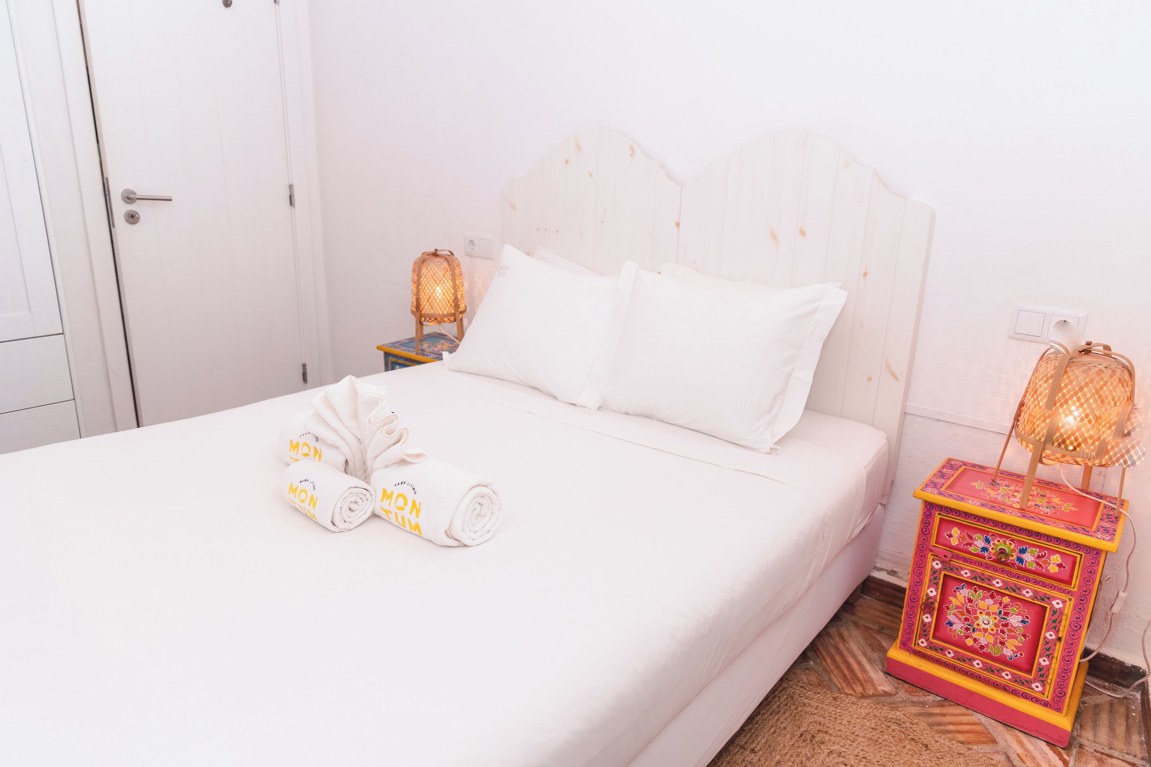 Habitación de hotel con cama, almohadas, una toalla enrollada, una mesita de noche con lámpara y una caja decorativa.