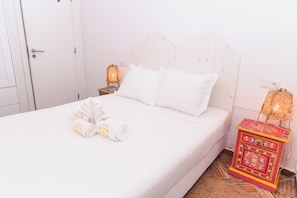 Habitación de hotel con cama, almohadas, una toalla enrollada, una mesita de noche con lámpara y una caja decorativa.