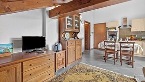 A kitchen with wooden cabinets, a dining table set for two, and a television on a wooden cabinet. - Alpine Loft Sommeiller (Bardonecchia)