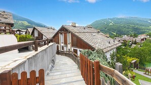 A traditional chalet-style building with a stone facade and wooden beams, surrounded by lush greenery and mountains. - Alpine Loft Sommeiller (Bardonecchia)