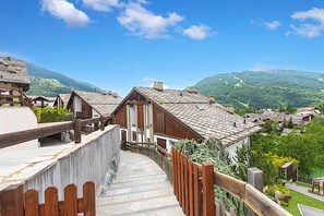 Ein Chalet im traditionellen Stil mit Natursteinfassade und Holzbalkonen, umgeben von üppigem Grün und Bergen.