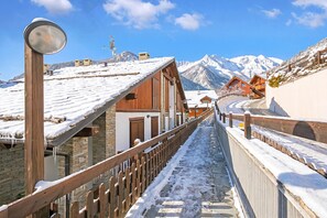 Ein verschneiter Holzsteg führt zu einem Bergdorf mit traditionellen Chalets.