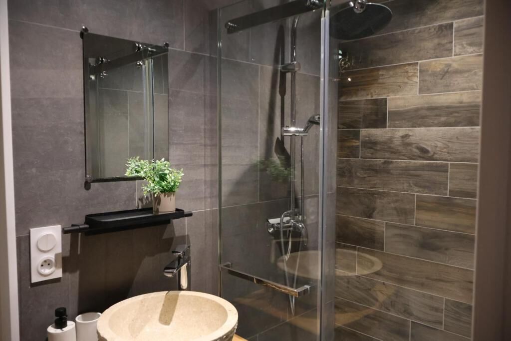 Un baño moderno con ducha de vidrio, un lavabo redondo y un espejo encima.
