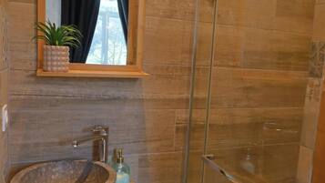 Un baño con lavamanos de piedra, un espejo, una planta en maceta y un box de ducha de cristal.