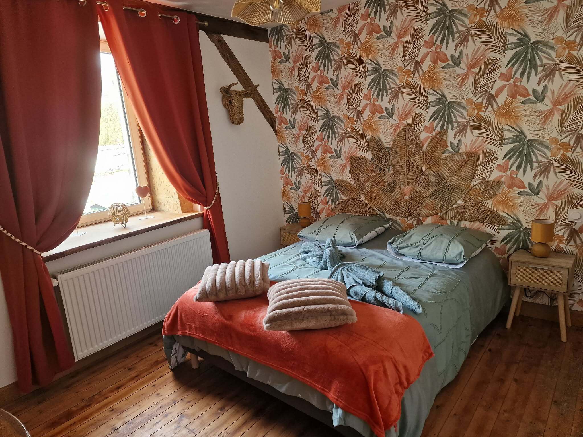 Un dormitorio con cama, ventana con cortinas, radiador y pared con diseño de hojas tropicales.