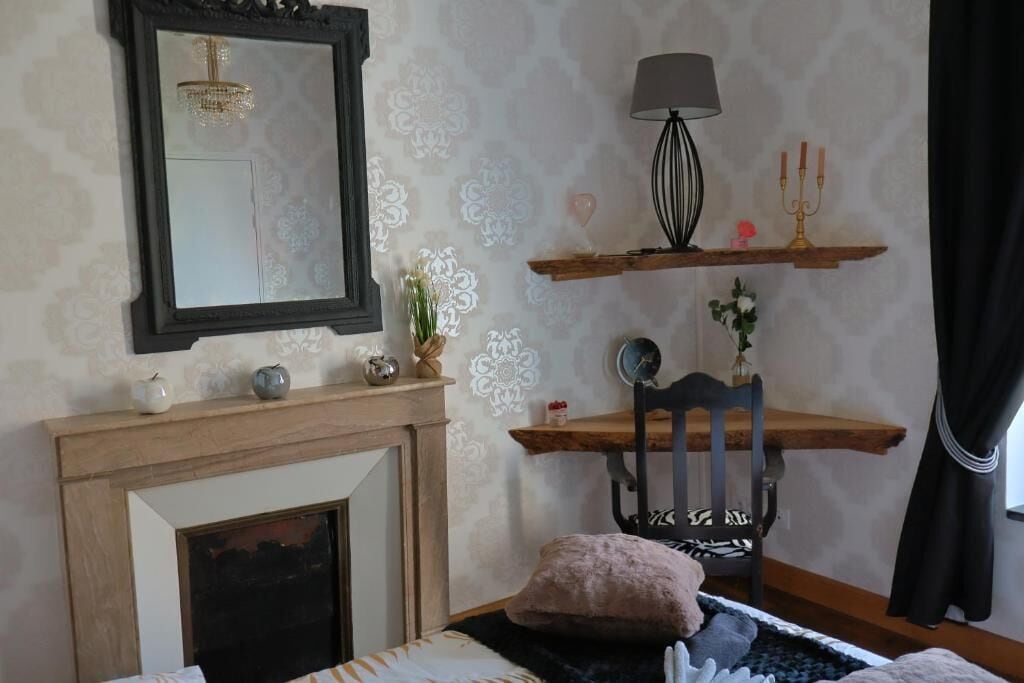 Ein Schlafzimmer mit Kamin, Spiegel, Lampe, Stuhl und Bett.