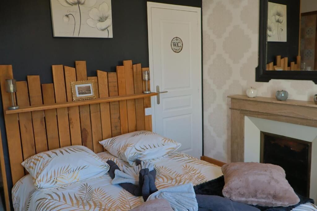 A bedroom with a wooden headboard, a bed with patterned bedding, a white door with a logo, and a fireplace with decorative items.