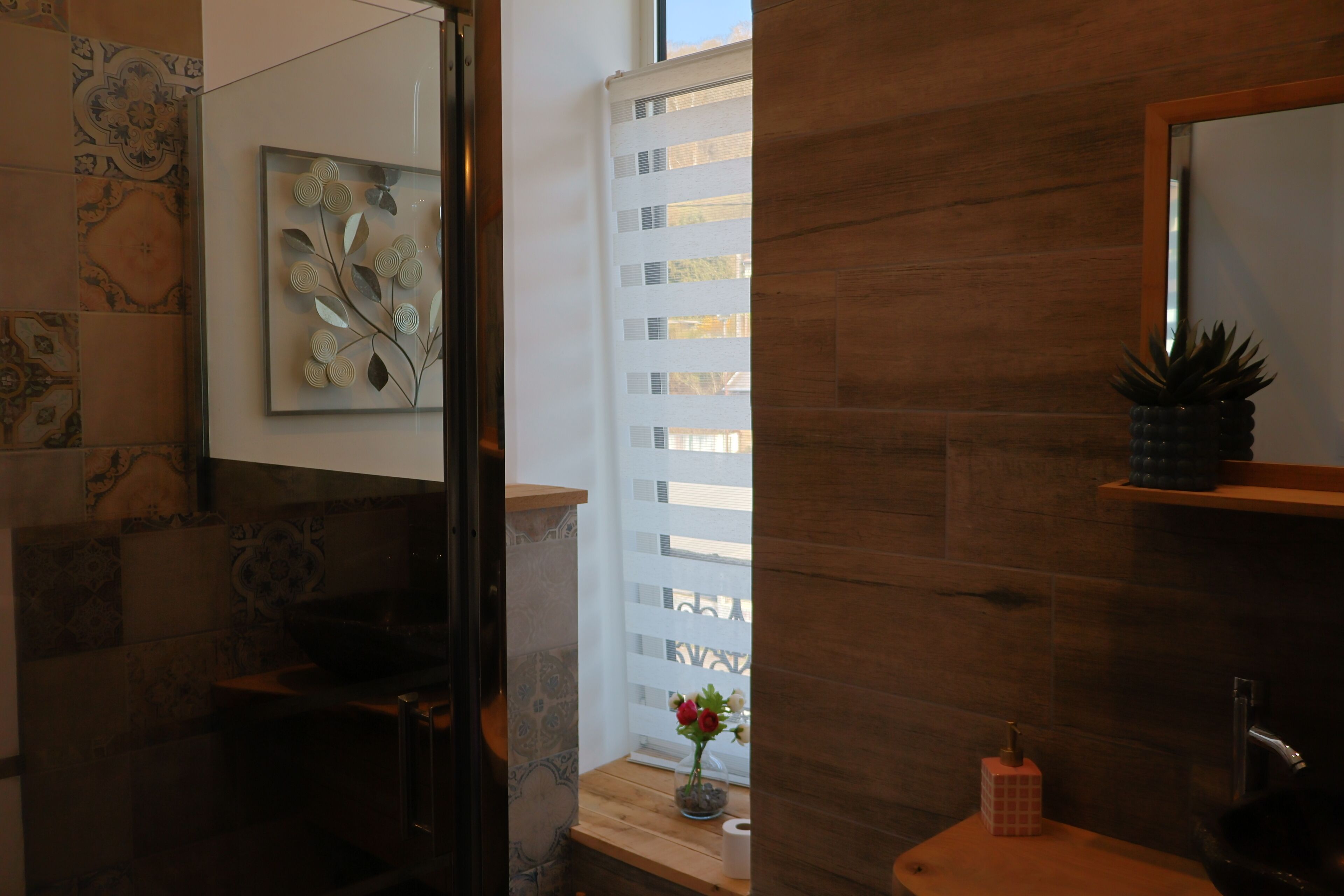 Une salle de bain avec un meuble-lavabo en bois, un miroir, un évier et une fenêtre donnant sur un immeuble.