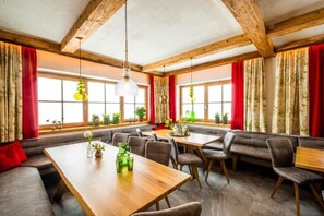A restaurant with wooden beams, large windows with red curtains, and a variety of seating arrangements including tables and benches. - Ferienhaus Mandlberggut by Apart4you (Radstadt)