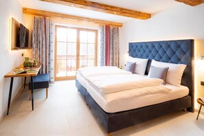 Ein Schlafzimmer mit einem großen Bett, einem Schreibtisch mit Stuhl, einem an der Wand befestigten Fernseher und einem Fenster mit Vorhängen.