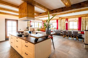 A spacious kitchen with wooden beams, a central island, and a dining area with red curtains.
