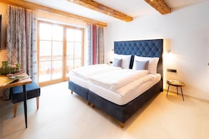A bedroom with a large bed, a desk, and a window with curtains.
