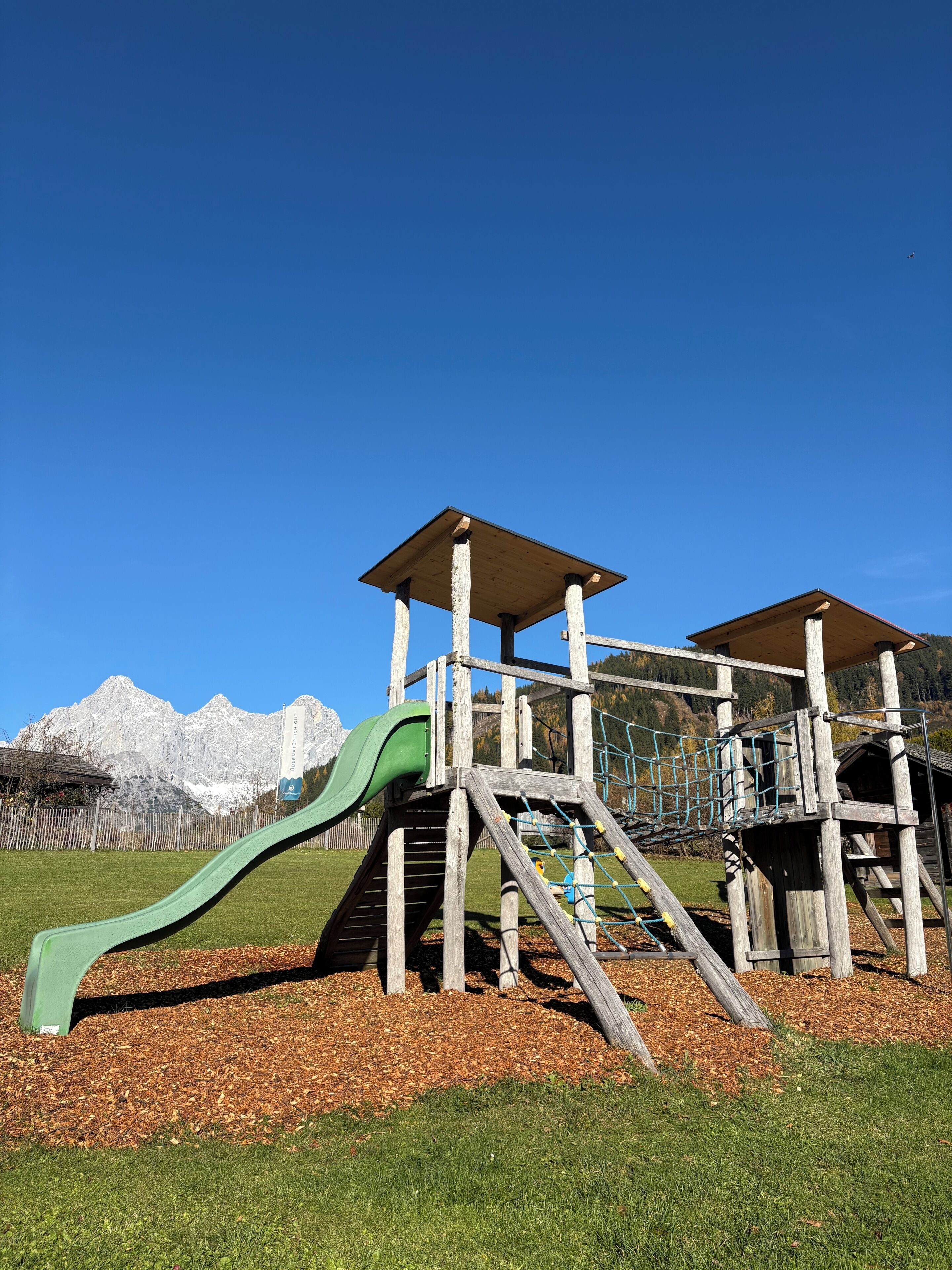 Un terrain de jeux avec un toboggan et des structures d’escalade, le tout situé dans un cadre magnifique, avec des montagnes en toile de fond.