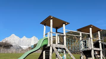Un terrain de jeux avec un toboggan et des structures d’escalade, le tout situé dans un cadre magnifique, avec des montagnes en toile de fond.