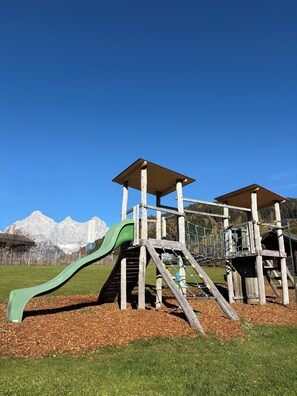 A playground with a slide and climbing structures, set against a backdrop of mountains.