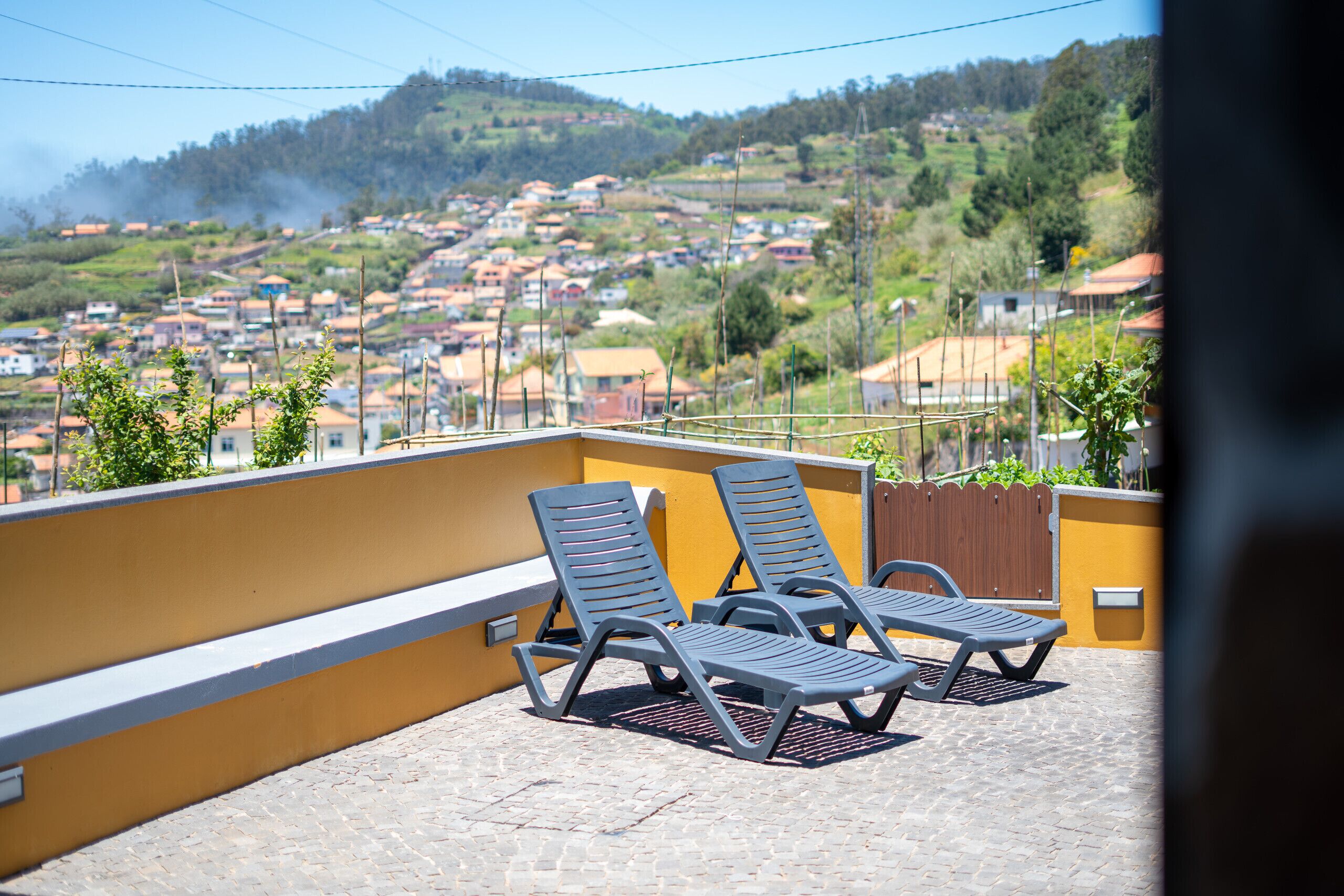 A balcony with two lounge chairs, a yellow wall, and a view of a residential area.