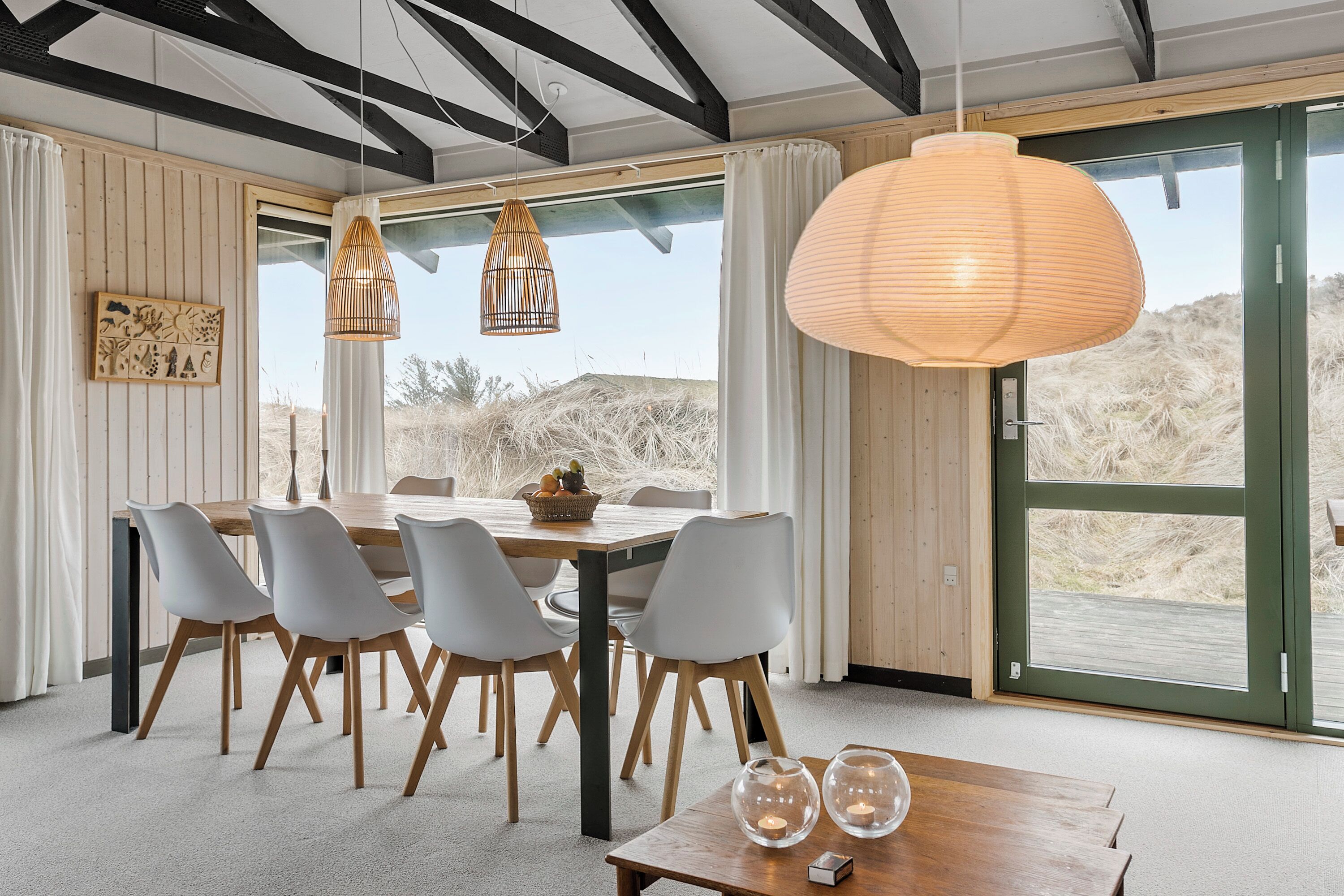 A modern dining area with a wooden table, white chairs, and pendant lights.