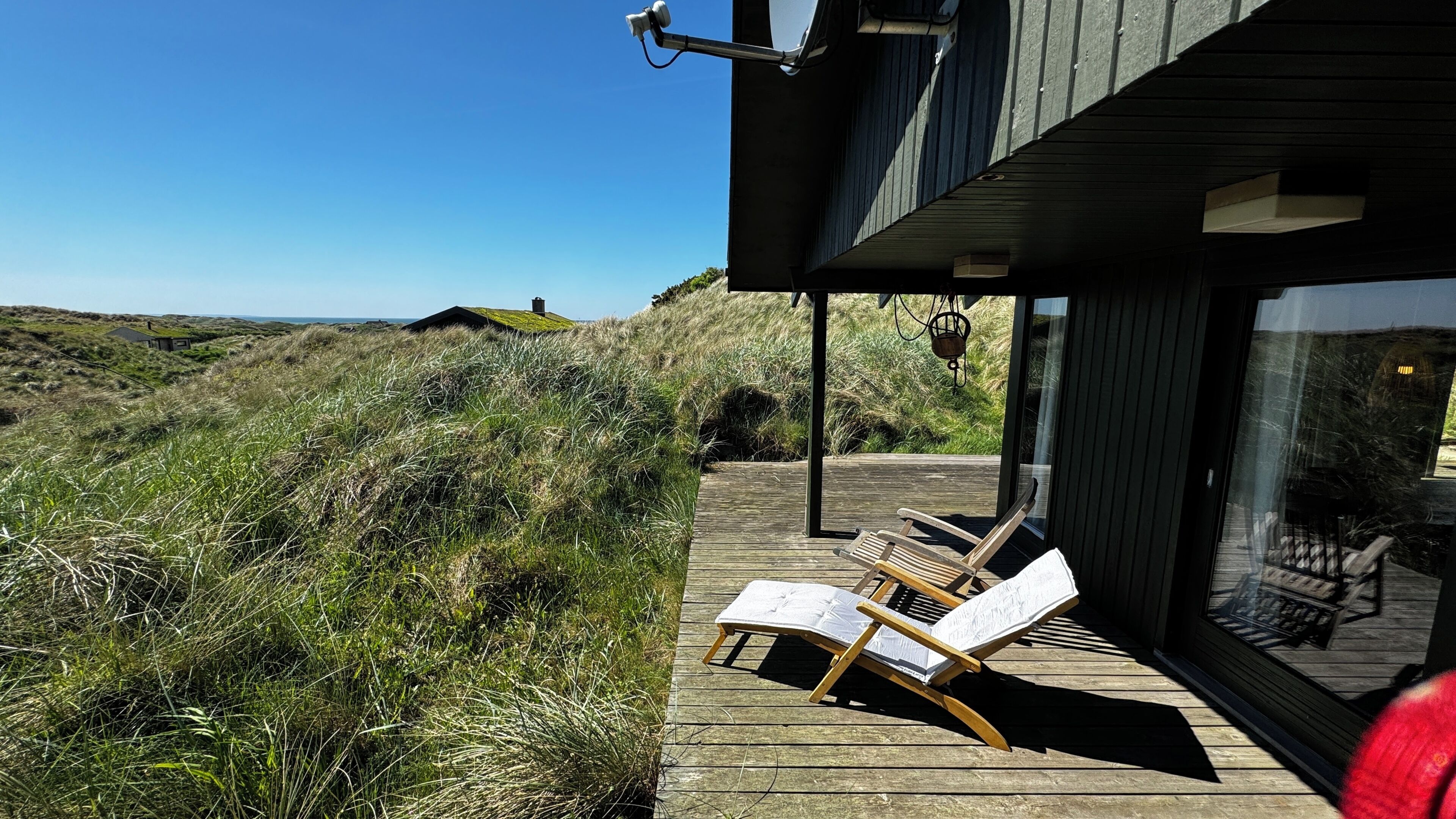 En træterrasse med to liggestole, med udsigt over et græslandskab med en bygning i baggrunden.