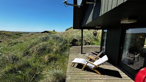 Ett trädäck med två solstolar, med utsikt över ett grönområde och en byggnad i bakgrunden.
