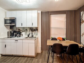 Une cuisine moderne avec des armoires blanches, un four à micro-ondes encastré et un coin repas comprenant une table et des chaises en bois.