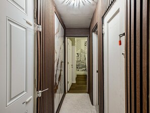 Ein Flur mit einer weißen Tür links, einer Holztür rechts und einer weißen Decke mit einer Leuchte.