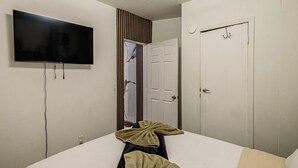 Un dormitorio con una cama, televisor montado en la pared, una puerta y un espejo.