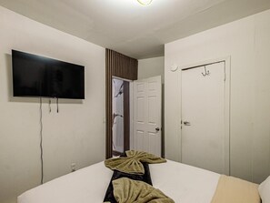 Ein Schlafzimmer mit einem Bett, einem an der Wand befestigten Fernseher, einer Tür und einem Spiegel.