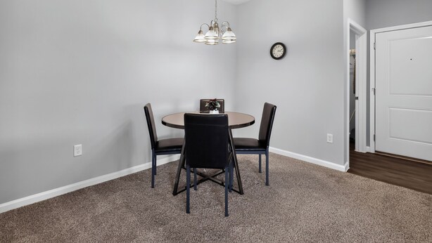 A dining area with a round table, four chairs, a chandelier, a clock, and a white door. - Fresh 1-bedroom layout (Princeton)
