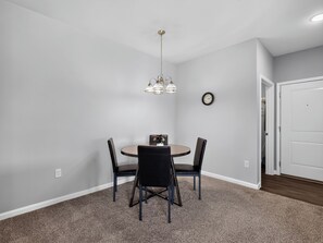 A dining area with a round table, four chairs, a chandelier, a clock, and a white door. - Fresh 1-bedroom layout (Princeton)