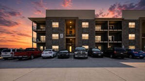 A multi-story parking garage with several cars parked in front of a building with balconies and a brick facade. - Fresh 1-bedroom layout (Princeton)