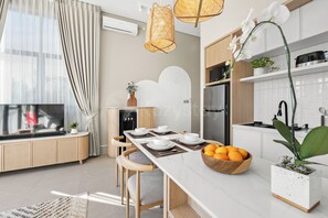 A modern kitchen with a dining area, including a refrigerator, sink, and a bowl of oranges. - Avelora Villa by Kozystay - Jimbaran (Badung)