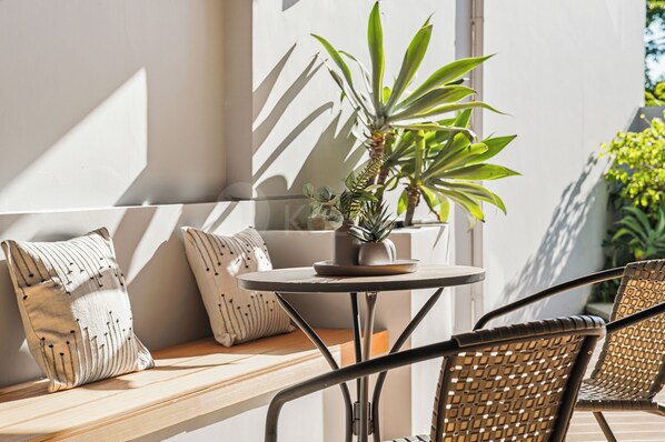 A sunlit outdoor seating area with a round table, a potted plant, and wicker furniture.