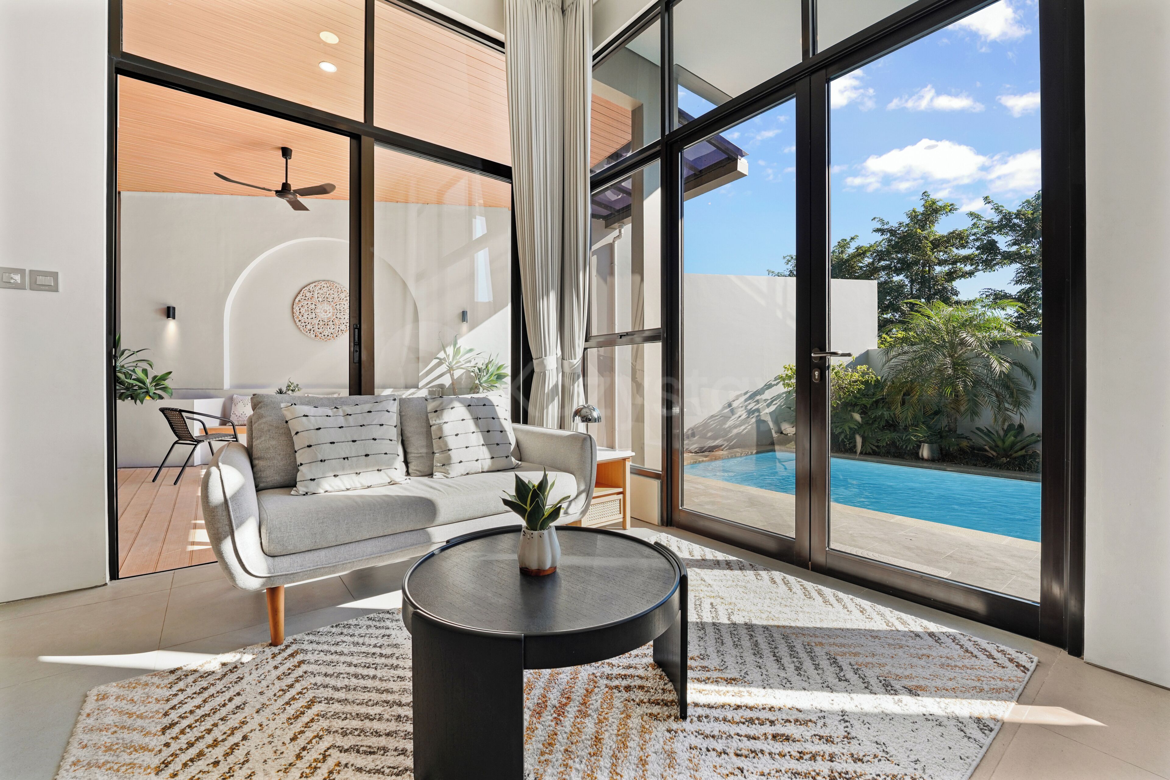 A modern living room with a sofa, coffee table, and large windows overlooking a pool.