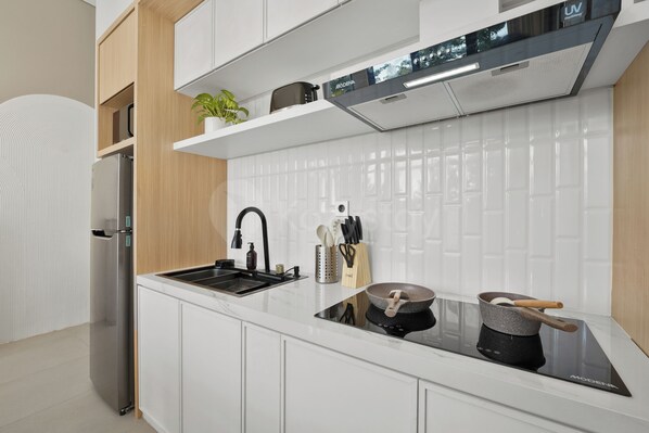 A modern kitchen with white cabinetry, a stainless steel refrigerator, a black induction cooktop, and a built-in oven.
