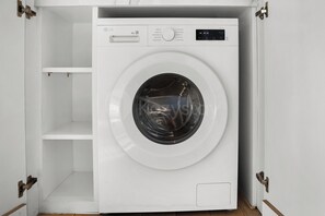 A white front-loading washing machine with a digital display, a control panel, and a small shelf below it.
