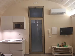 A compact kitchen with a microwave, a sink, and a small table with a phone and a bottle. - Apartment in the heart of the city (Taranto)