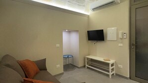 A living room with a stone ceiling, a flat-screen TV mounted on the wall, a white bench, and a door. - Apartment in the heart of the city (Taranto)
