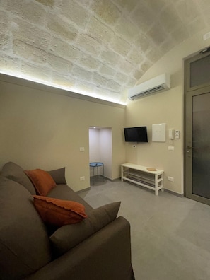 Ein Wohnzimmer mit Steindecke, einem an der Wand befestigten Flachbildfernseher, einer weißen Bank und einer Tür.