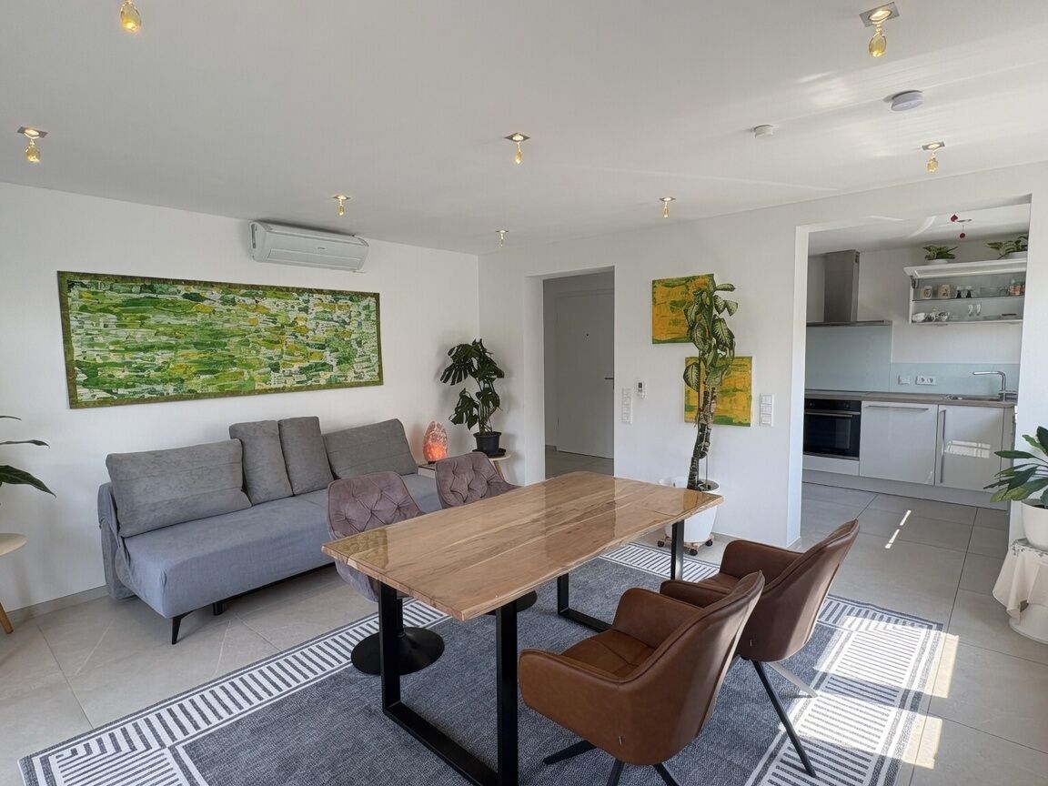 Un salon moderne avec un canapé, une table à manger et des chaises. On aperçoit une cuisine à l’arrière-plan.
