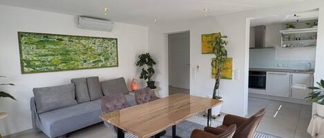 Un salon moderne avec un canapé, une table à manger et des chaises. On aperçoit une cuisine à l’arrière-plan.