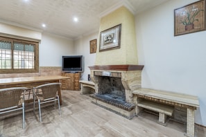 A room with a fireplace, a television, a dining table with chairs, and a window with a view.