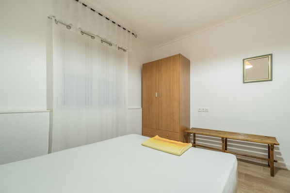 A bedroom with a bed, a wooden wardrobe, a bench, and a mirror on the wall.